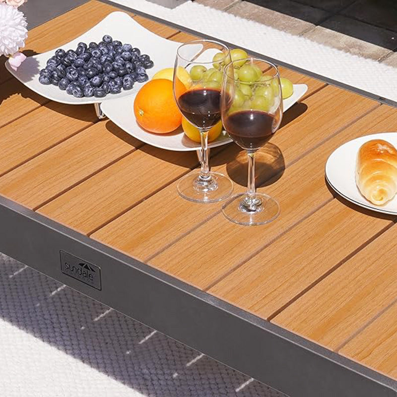 Wooden finished coffee table with fruit, wine glasses, and pastries on a patio.