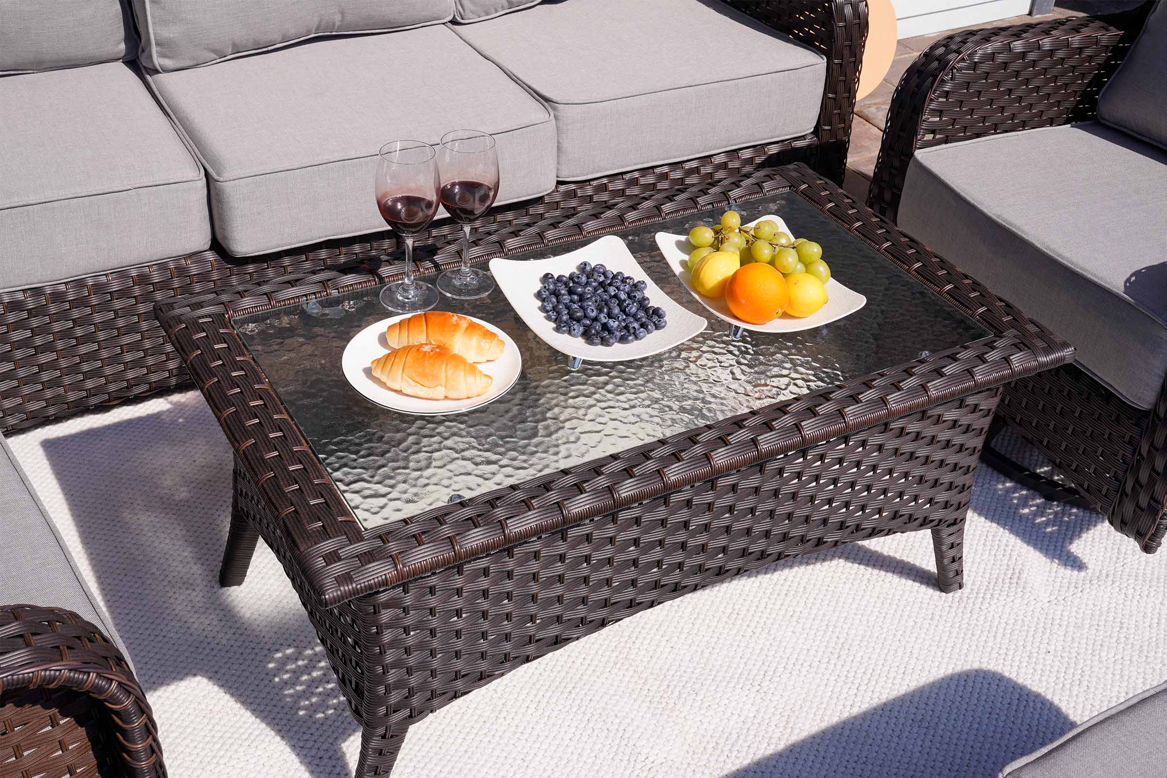 Outdoor patio set with a glass-top coffee table featuring food and drinks.