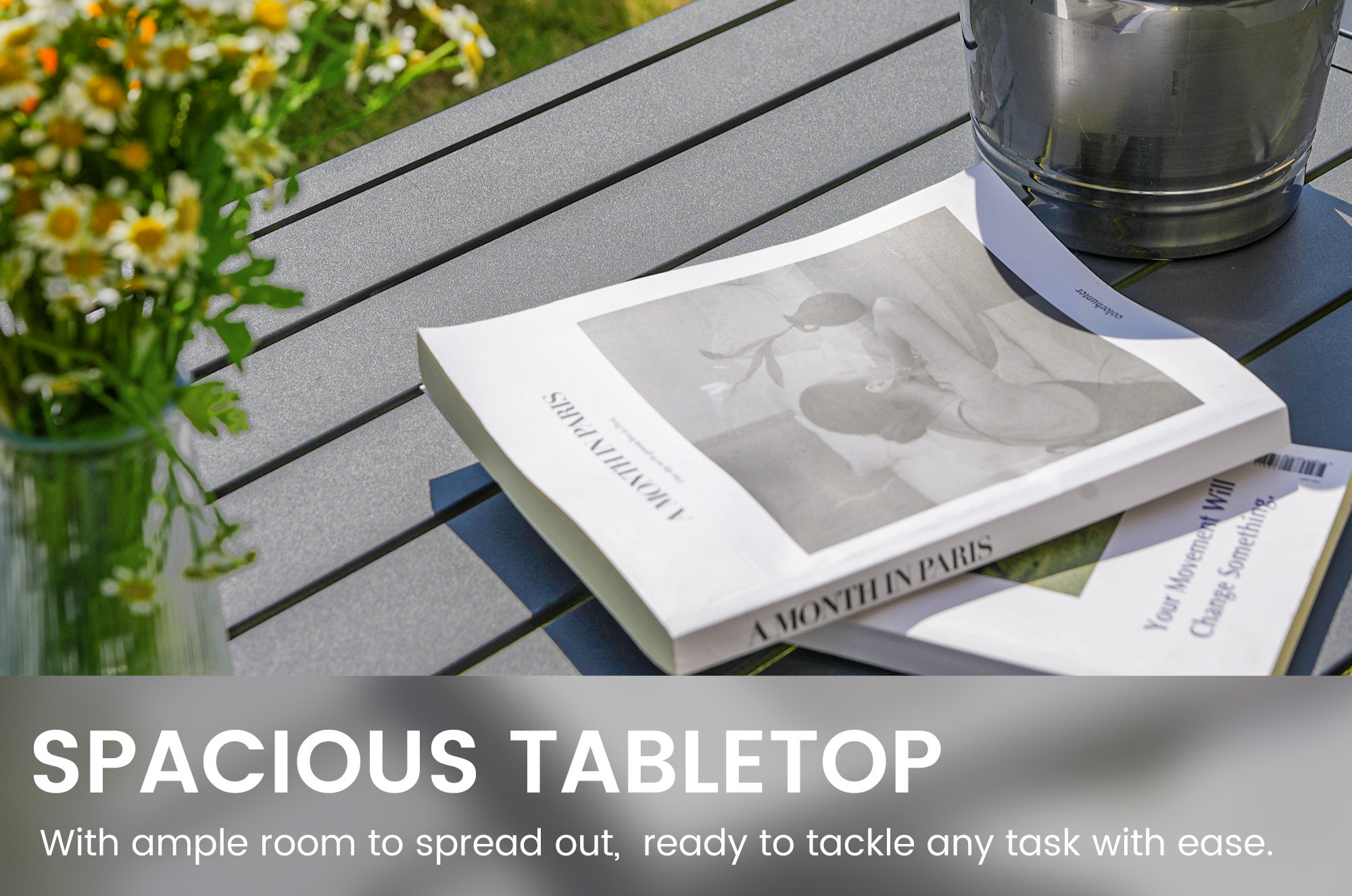 Books and a vase on a spacious outdoor table with flowers.