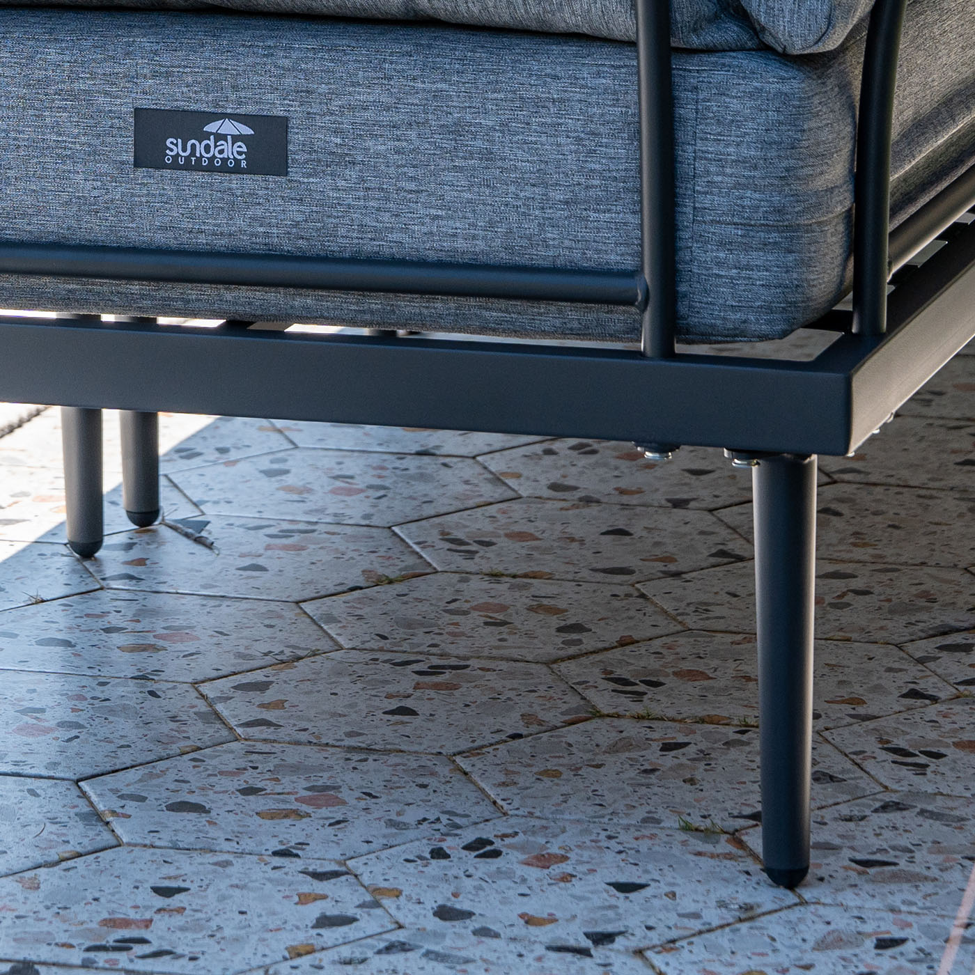 Gray outdoor sofa with metal frame on a stone patio, featuring 'Sundale Outdoors' logo.