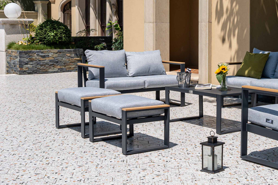 Outdoor patio furniture set with gray cushions and wooden accents on a stone patio.