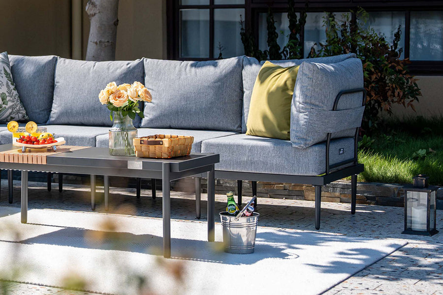 Outdoor patio set with gray sofa, coffee table, and decorative items on a sunny day.