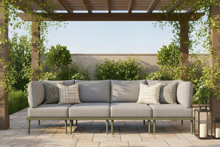 Outdoor patio with a gray sofa under a pergola, surrounded by greenery.