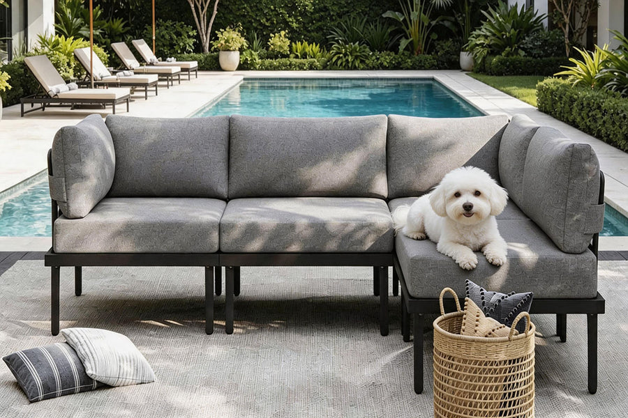 Gray outdoor sectional sofa with a dog sitting on it, surrounded by a pool and garden.