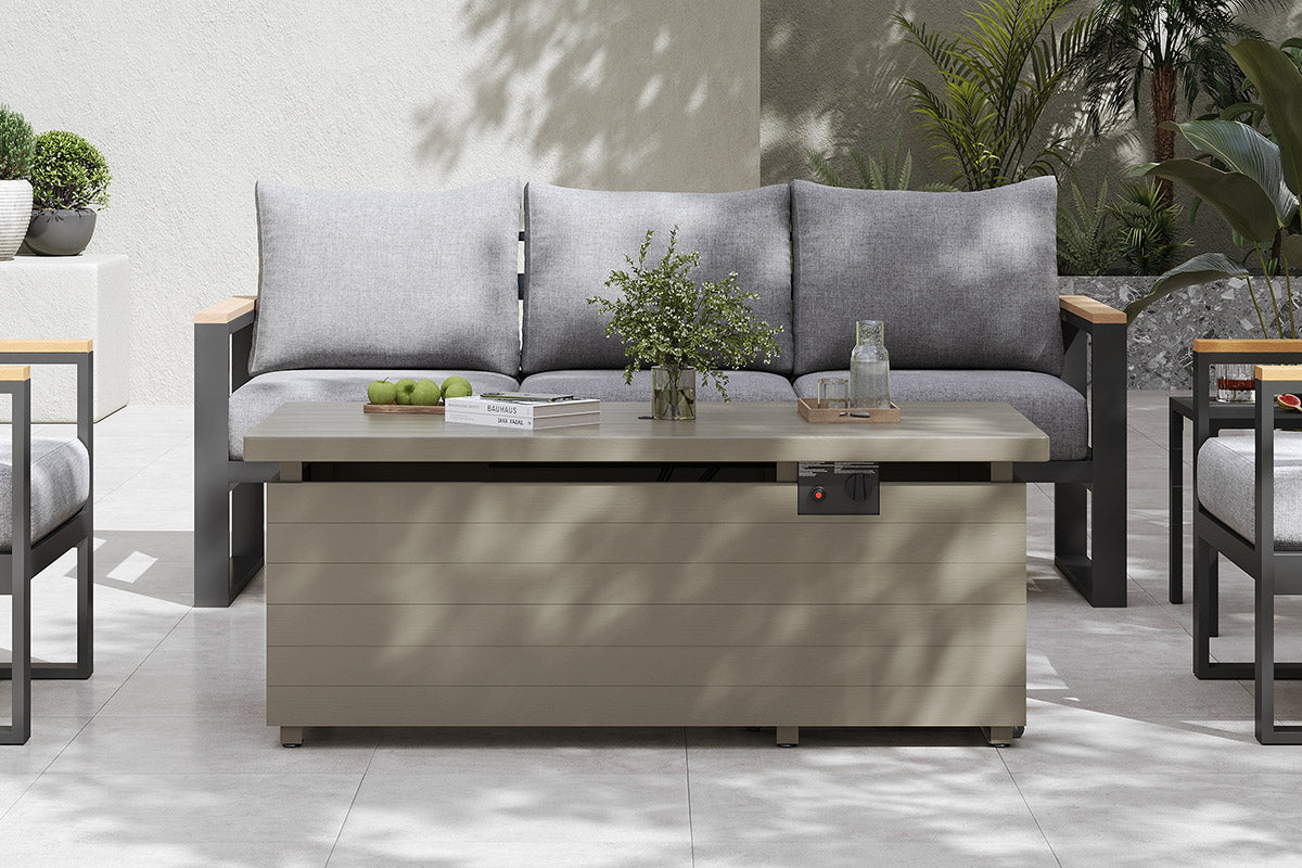 Outdoor patio set with gray sofa and wooden coffee table in a garden setting.#color_green