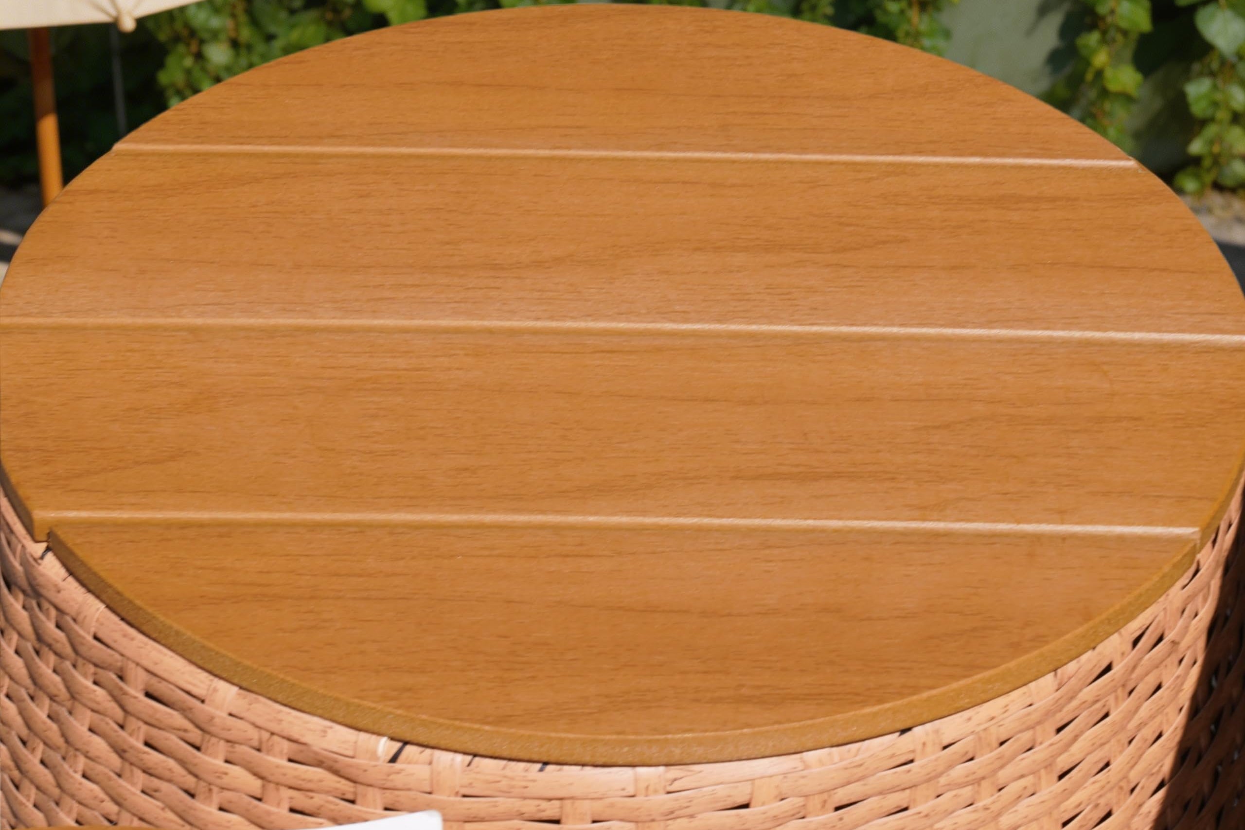 Round wooden table with wicker base outdoors, featuring a magazine and croissant.