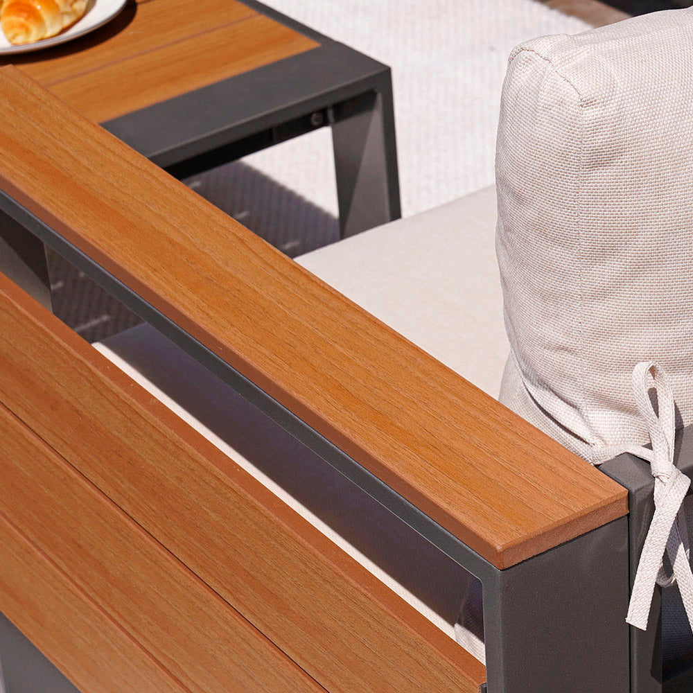 Close-up of a wooden outdoor table with a cushioned chair in the background.