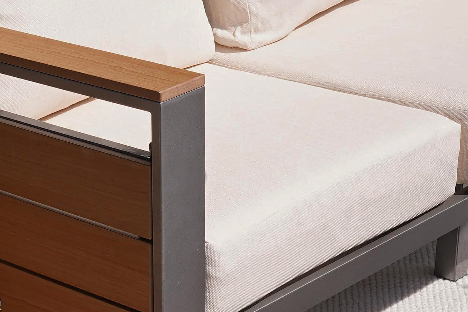 Close-up of a modern outdoor sofa with wooden grin armrests and aluminium frame.#color_beige