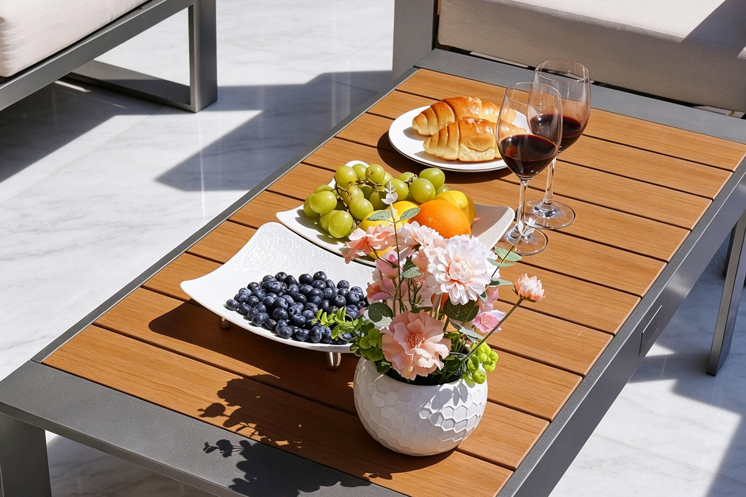 Wooden outdoor table with fruit, flowers, and croissants on a patio.#color_beige