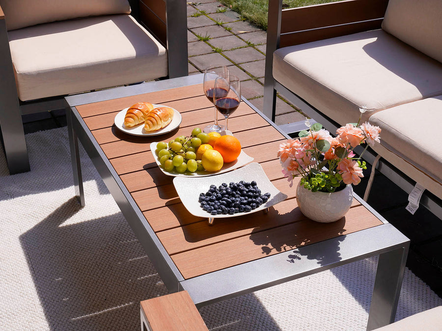 Outdoor setting with a coffee table, chairs, and a plate of food including fruits and pastries.