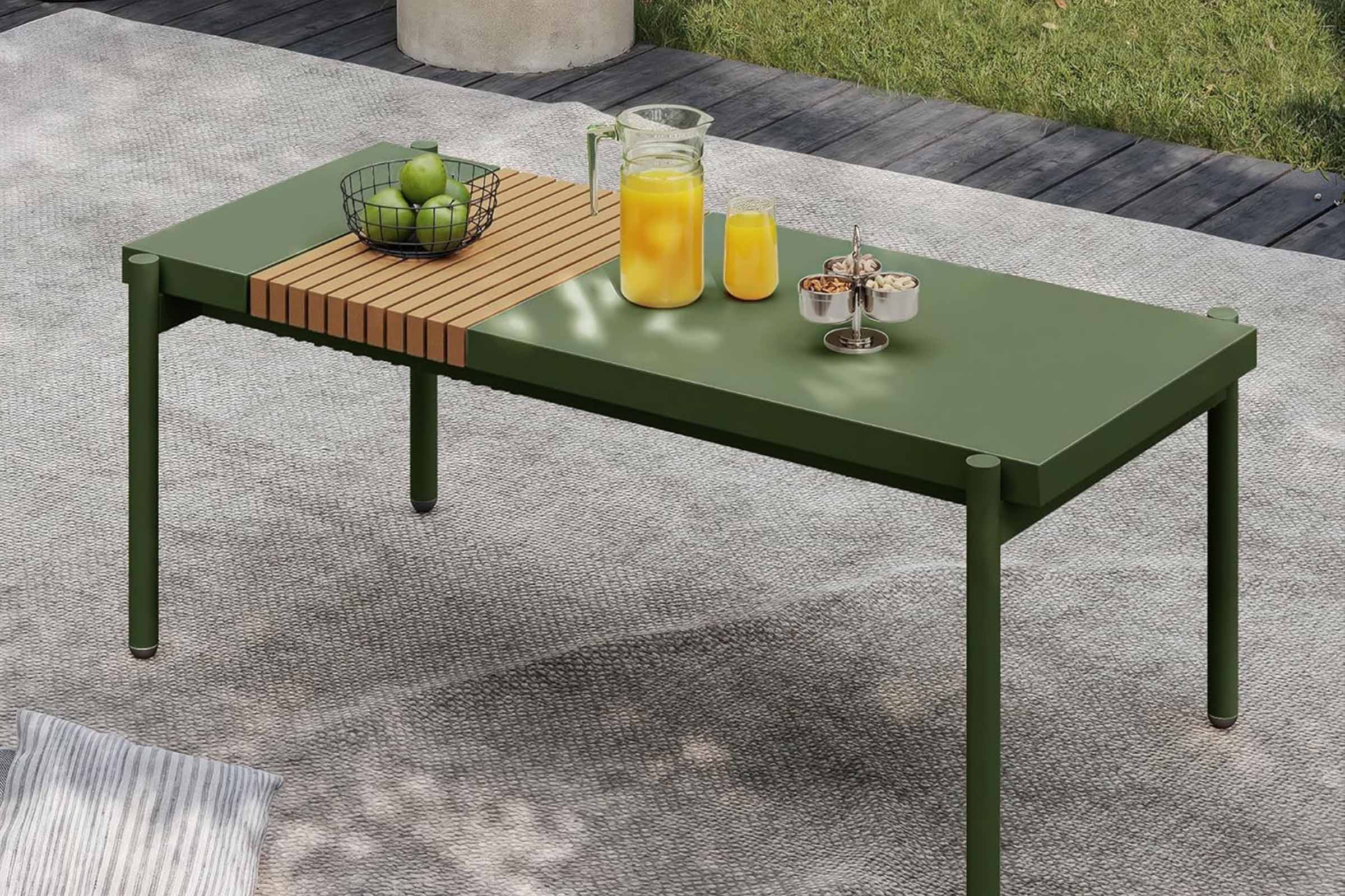 Green outdoor table with a wooden top, fruits, and drinks on a patio.#color_green