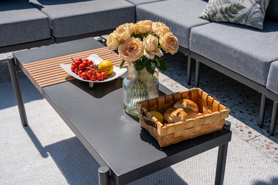 Outdoor coffee table with fruit, flowers, and bread on a patio.#color_gray