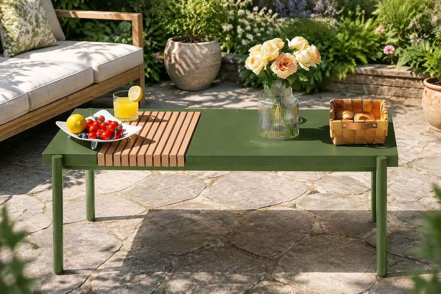 Green outdoor table with a wooden slatted side, fruit, and flowers on a stone patio.