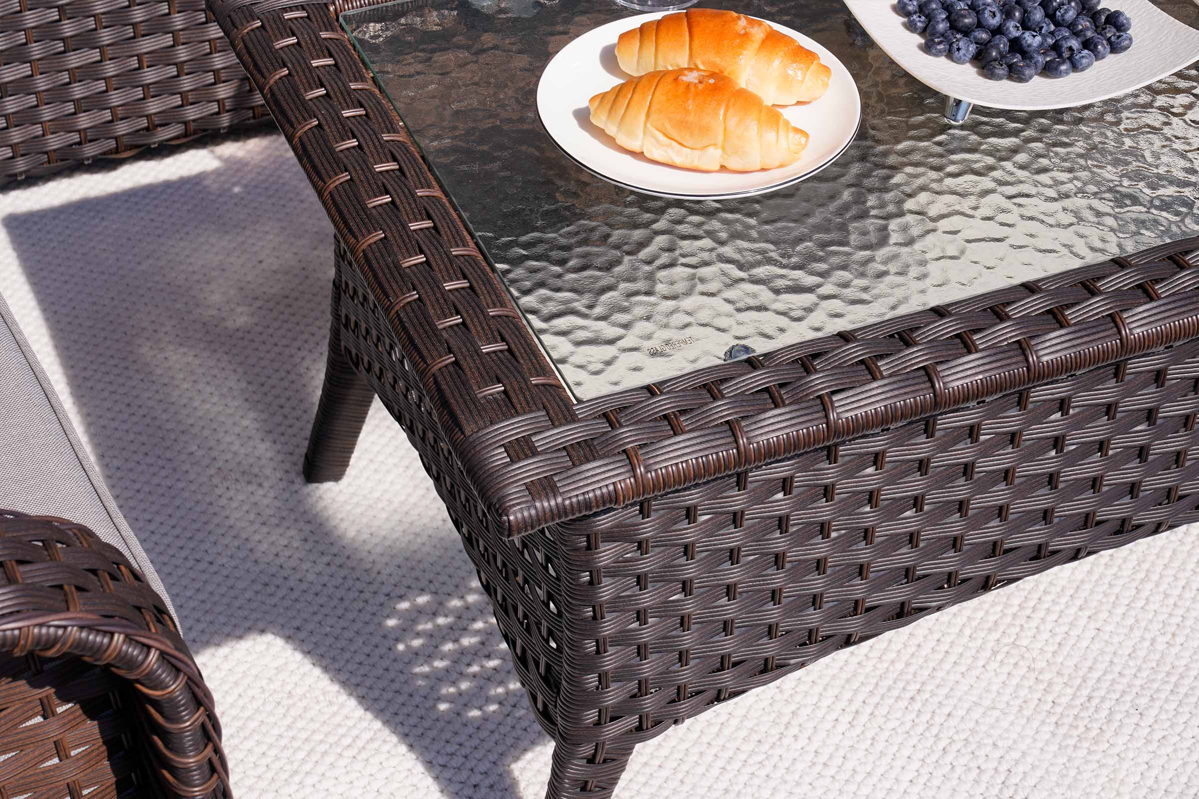 Wicker outdoor table with a glass top, featuring pastries and blueberries on a white surface.