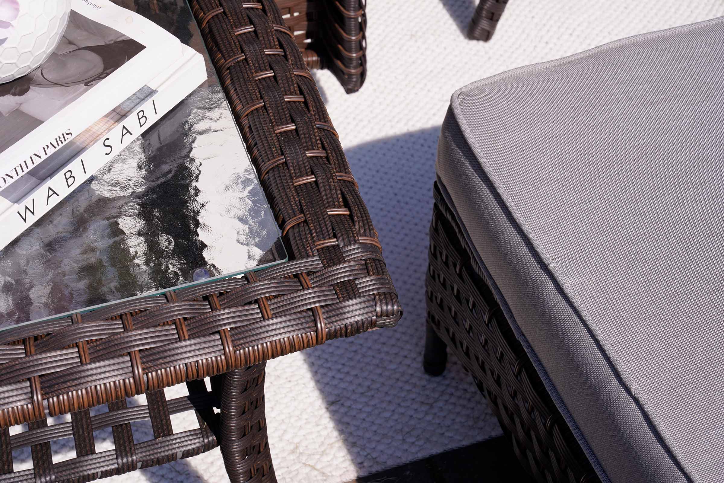 Wicker table with a glass top and a gray cushioned chair on a textured surface.